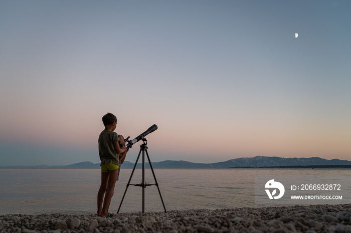 Brothers standing on beautiful pebble beach looking to the stars with a telescope