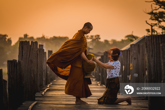 Asian buddha religion lady giving food to monk in early morning  to pay respect to Buddha is do good things for Buddhist at U-bein bridge , Myanmar.