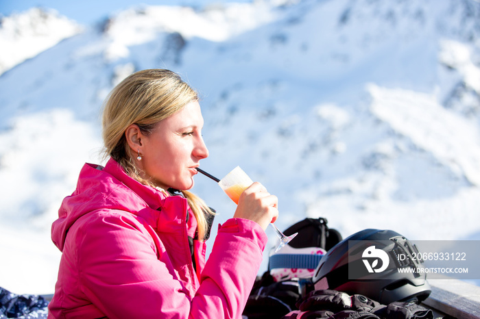 Young woman, drinking alcohol egg punch bombardino on a ski break on a sunny day in mountains