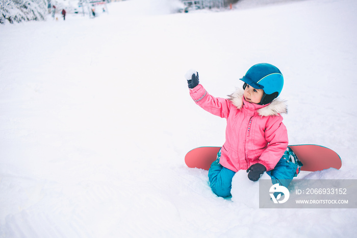 Snowboard Winter Sport. Little kid girl playing with snow wearing warm winter clothes. Winter background