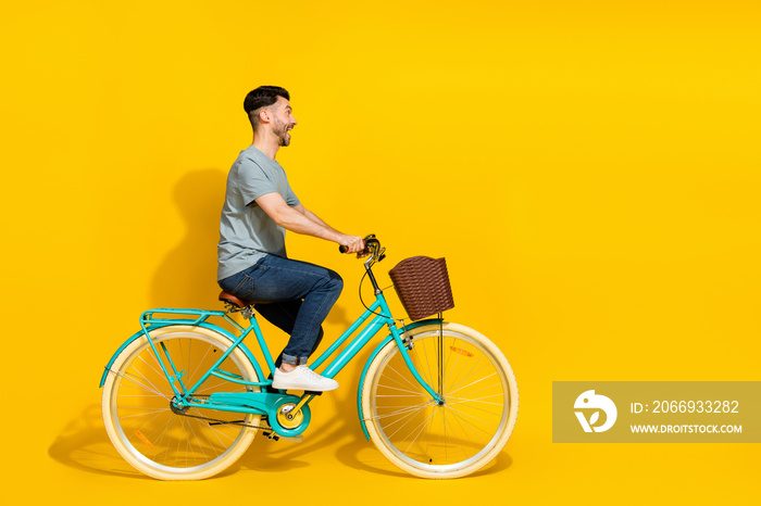 Side profile photo of young funny excited man riding bicycle crazy fast speed looking empty space spring vibes isolated on yellow color background