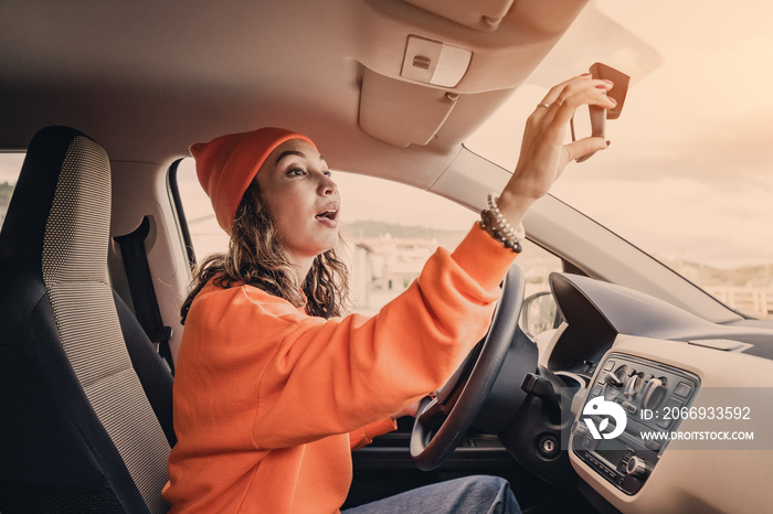 A teenage female driver corrects the rearview mirror in the car