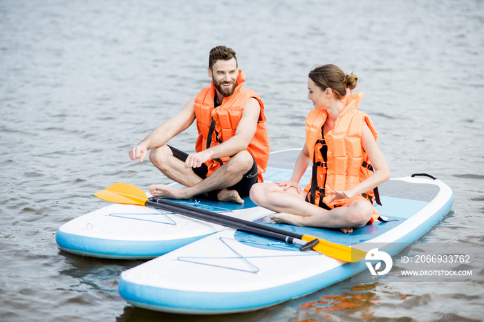 Couple in life vest relaxing on the stand up paddle board doing yoga