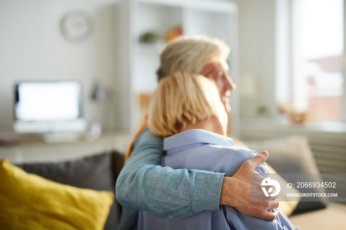 Back view portrait of happy senior couple embracing sitting on sofa at home, copy space