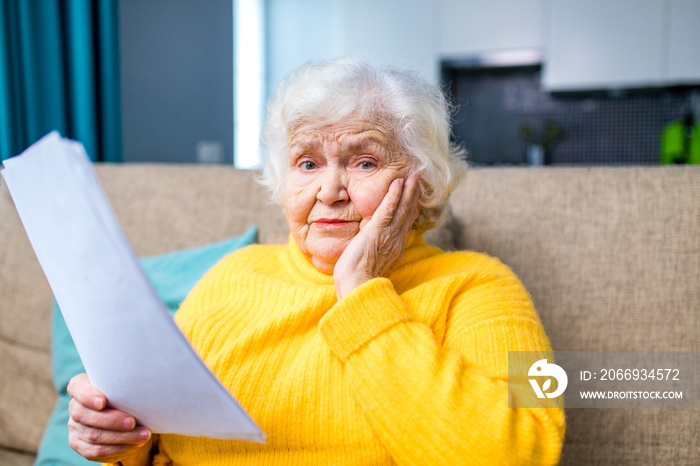 shoked amazed old woman white gray-haired sitting on the sofa in living room with laptop and bills