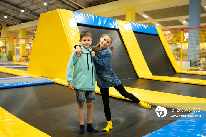 Happy smiling 11 years old kids jumping on trampoline indoors in entertainment center. Active children leisure, jumping and playing on trampoline in sport center. Amusement park. Sport activity