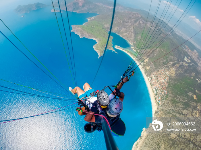 Paraglider tandem flying over the sea with blue water and mountains in bright sunny day. Aerial view of paraglider and Blue Lagoon in Oludeniz, Turkey. Extreme sport. Landscape