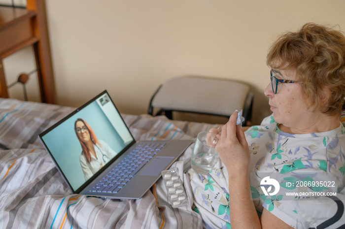 An elderly woman is talking with a doctor on Skype. A pensioner suffers from a respiratory disease and blows her nose. Online consultation.