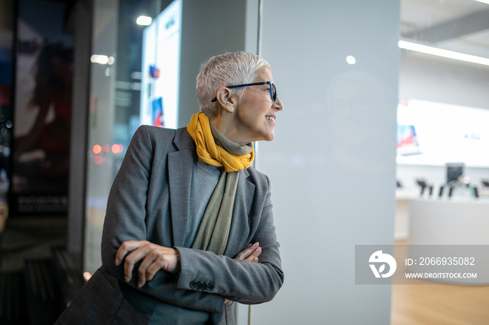 Smiling mature senior woman with short gray hair and eyeglasses walking on street, night scene in city