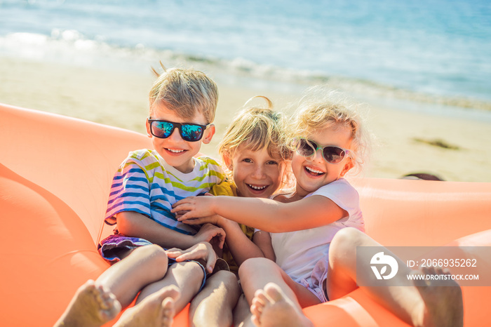 Children sit on an inflatable sofa against the sea and have fun