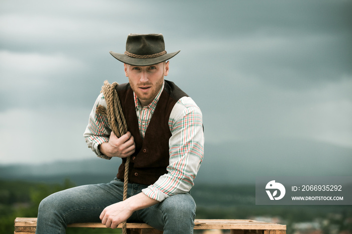 Cowboy with lasso rope on sky background. Western man with cowboy hat.