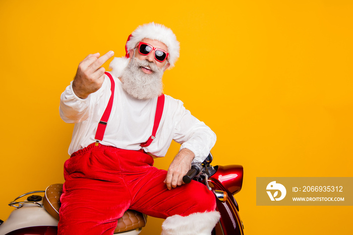 Photo of crazy white grey hair santa sitting on bike showing impolite gesture careless mood bad person wear sun specs pants cap shirt isolated yellow color background