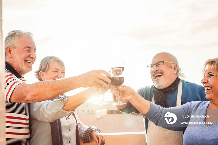 Happy seniors friends drinking red wine on terrace sunset - Pensioners people having fun enjoying time together outdoor - Elderly retirement lifestyle concept