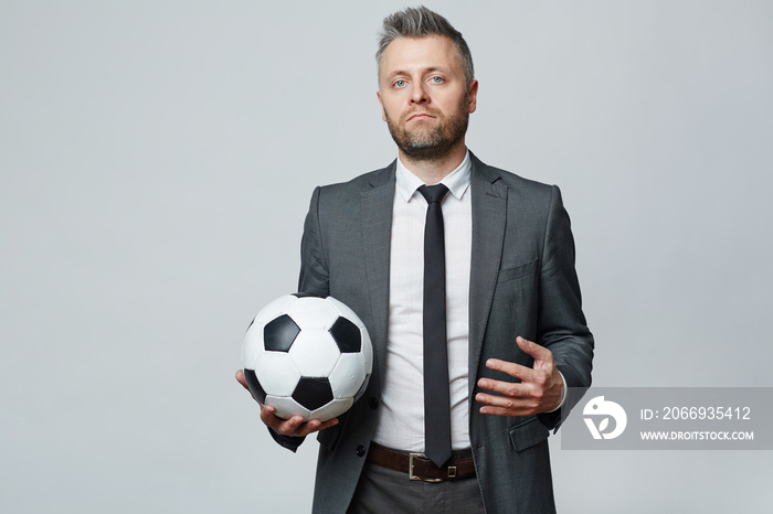 Waist up studio portrait of middle aged man with grey hair holding soccer ball and looking at camera