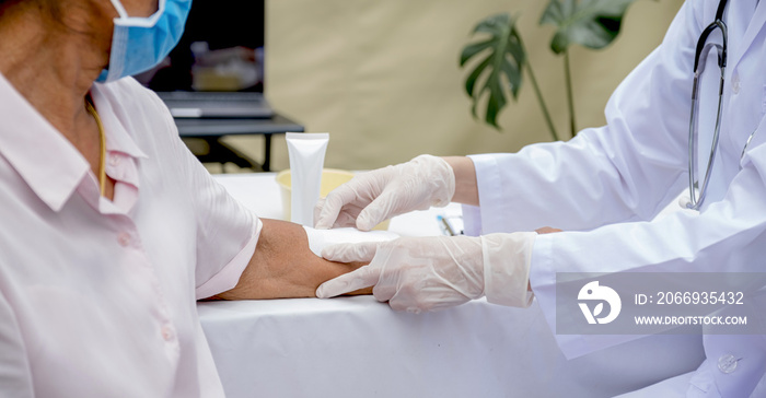 The doctor’s hand is making a wound on the arm of an elderly woman who has an accident