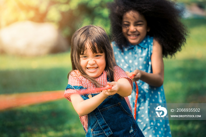 Happy children playing tug of war and having fun during summer camping in the park. Children recreation concept.