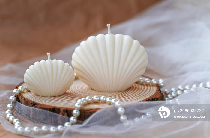 Handmade candles in the shape of a shell. Soy beige candles on wood, tulle and pearl background. Decor