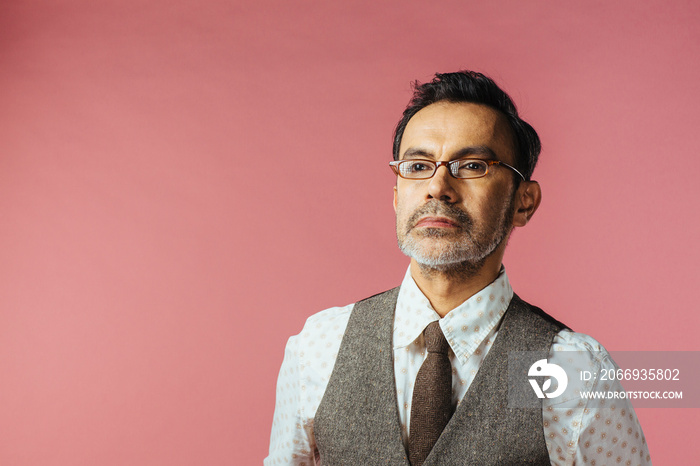 Portrait of a mature man in vest and glasses, isolated on pink