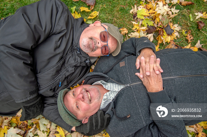 Gay senior married couple laying on the grass in an intimate moment taking a break from their back yard cleanup.