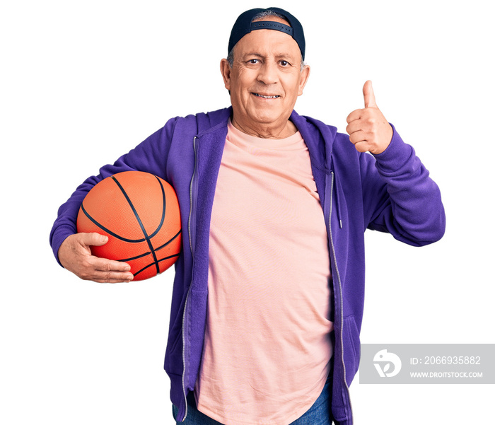 Senior handsome grey-haired man holding basketball ball smiling happy and positive, thumb up doing excellent and approval sign