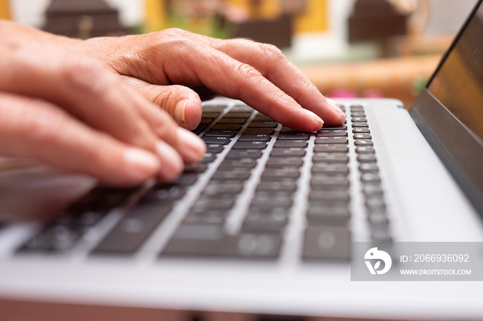 Mature woman’s hands typing on laptop keyboard browsing the net