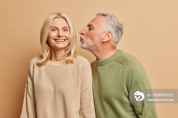 Love lives together. Loving caring husband going to kiss wife in cheek have good relationships pose for family portrait against brown background. Old couple pose indoor. Happy romantic mature woman