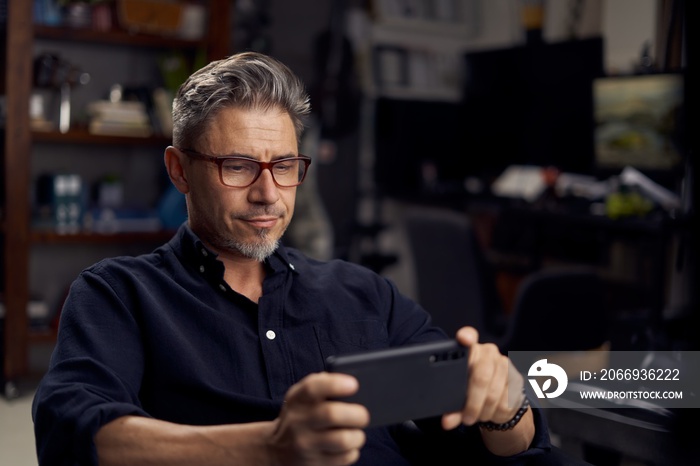 Man using smart phone at home sitting in armchair in cosy living room.