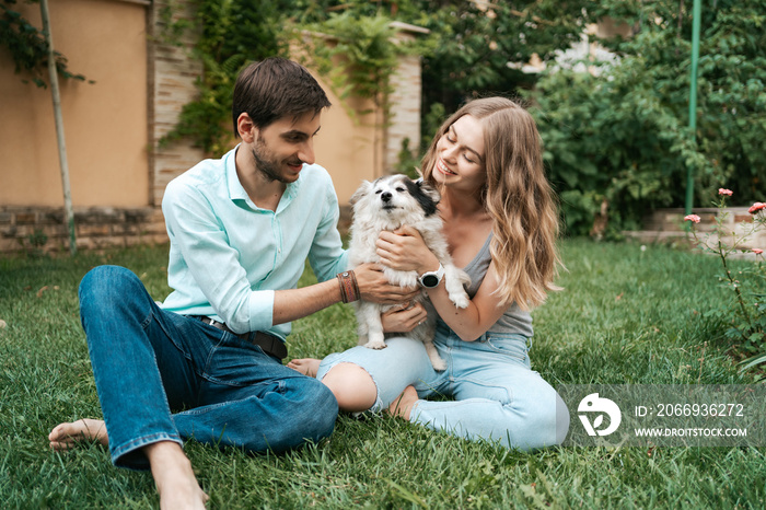 Happy couple of guys playing with their dog in the backyard on the grass. Cheerful old dog