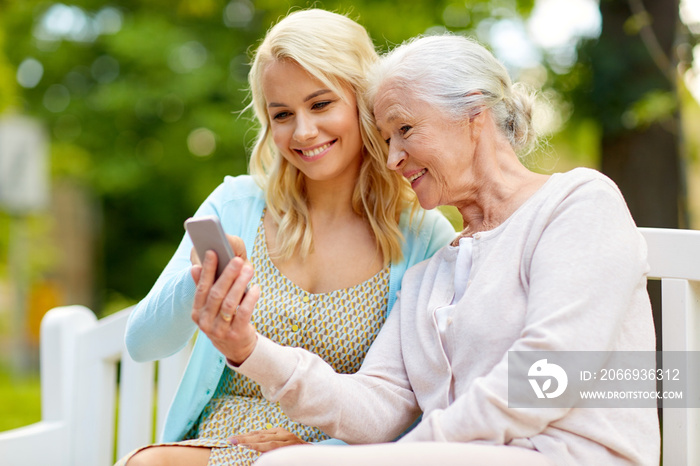 daughter and senior mother with smartphone at park