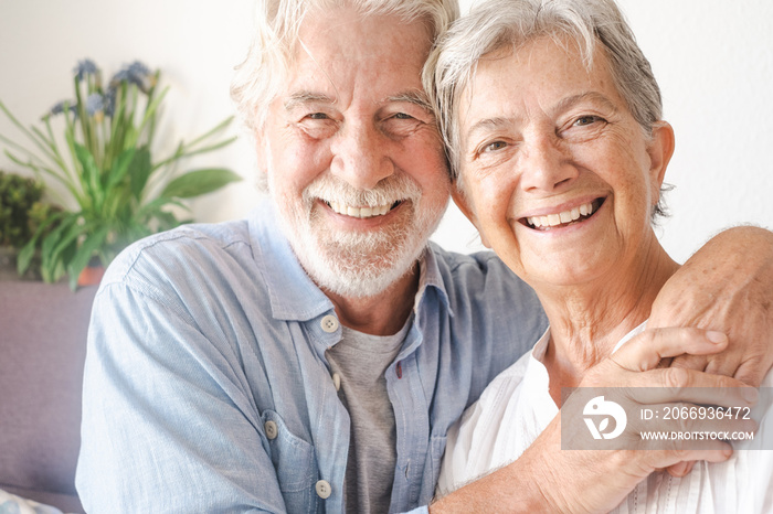 Smiling beautiful senior couple sitting on couch at home looking at camera