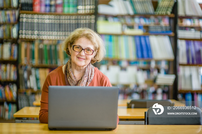 Happy senior woman using laptop in library. Space for text