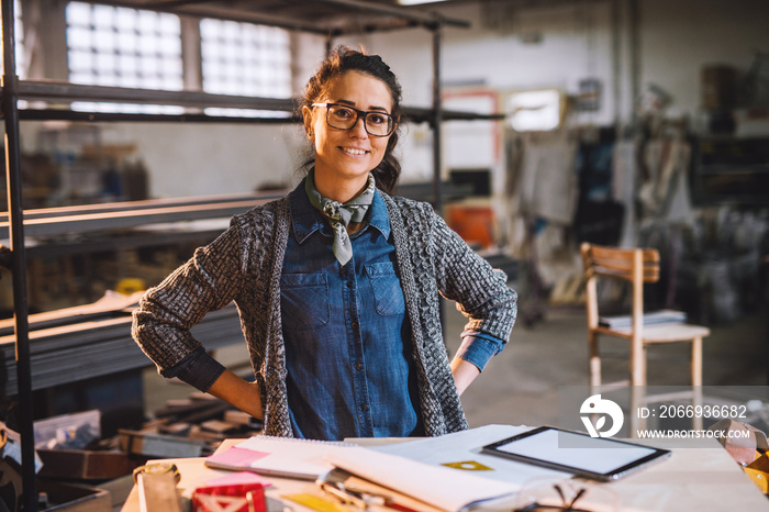 Portrait of cheerful happy middle aged engineer in sunny fabric workshop and posing behind the desk with tools.