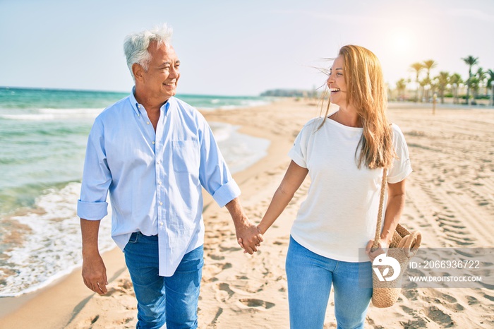 Middle age hispanic couple smiling happy walking at the beach.