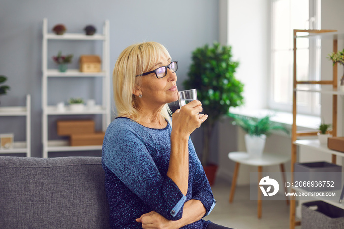 Pensive senior woman drinking a glass of pure fresh water to stay hydrated and healthy