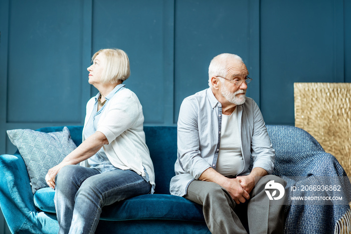 Offended senior man and woman feeling sad, sitting back to each other on the couch at home