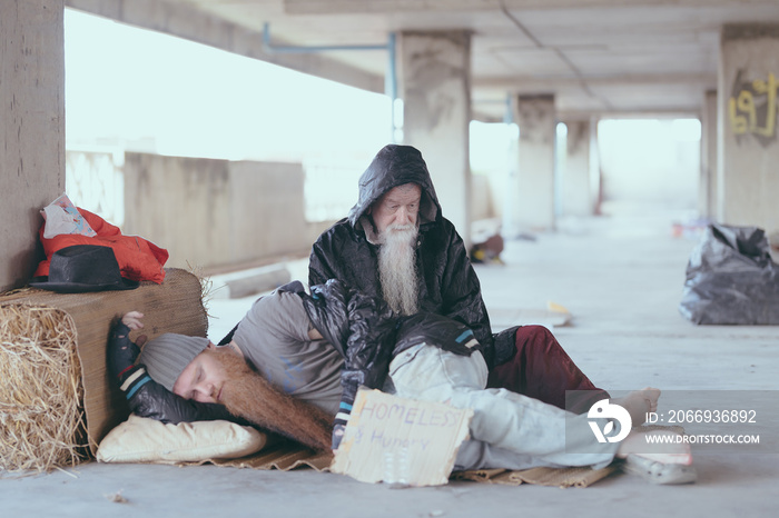 An old homeless man wearing a sweater and blanket sleeps on cardboard looking for help because of hungry beggars and food from passersby on the streets, homeless poor people and depression concepts.