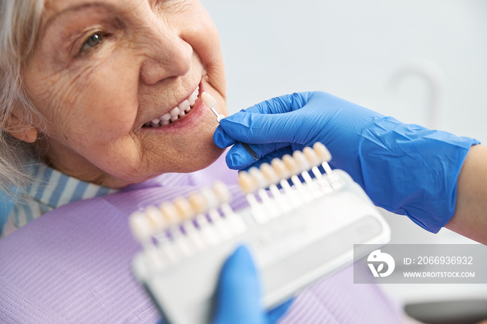 Person keeping a tooth shade next ot lady teeth