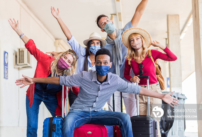 Multiracial group of friends at train station with luggage wearing protective mask. Tourism and holidays concept during Covid19 pandemic lockdown.