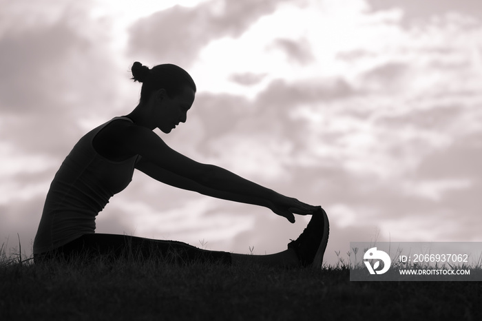 silhouette of young woman doing stretching exercise on background of sunset sky