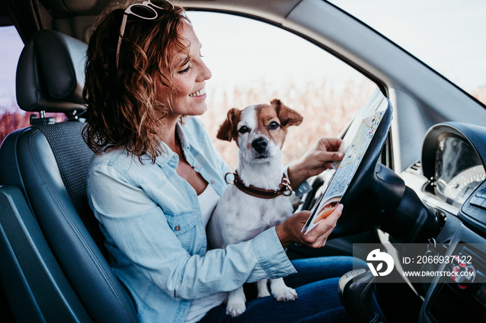 young beautiful woman reading a map in a car. travel concept. cute jack Russel dog besides.