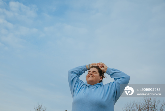 plus size woman with hands over head against blue sky