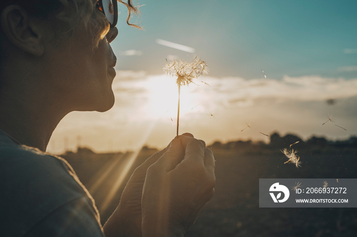 Day dreaming leisure activity with woman blowing a dandelion outdoor in the nature park. Emotion and love lifestyle people concept. Freedom and travel dreams. Sky and sunset in background