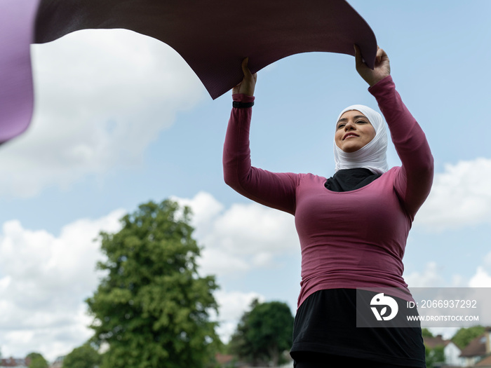 UK,Sutton,Woman in headscarf unrolling yoga mat outdoors