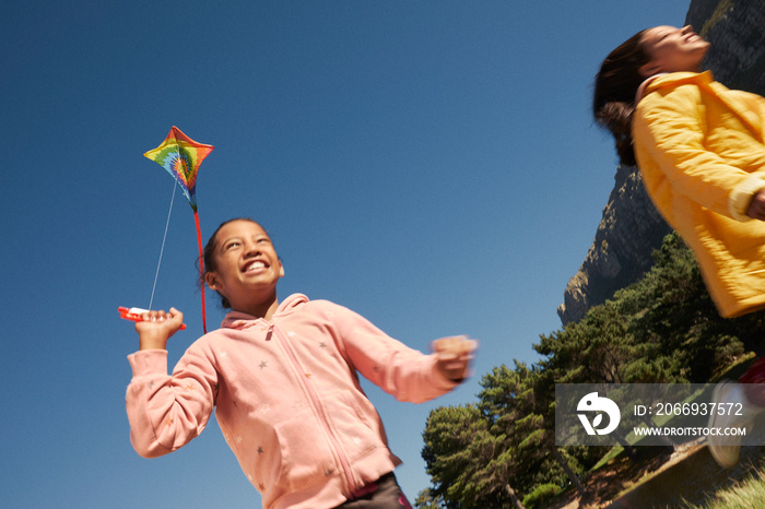 Little girls laughing and running while flying kites during family camping trip against blue sky