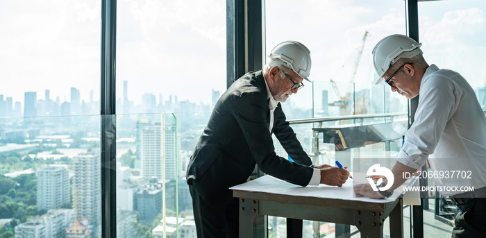 Two Engineer or Architect are analyzing blueprints while working on a new project on construction site with blue sky and city background.Architect supervising construction on terrace tower.