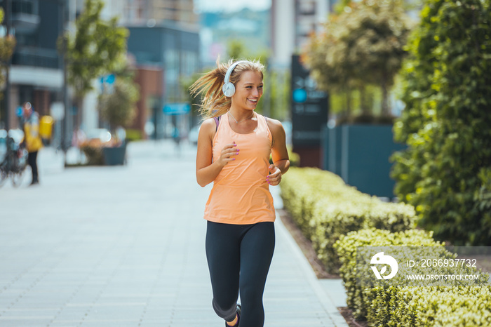 Healthy woman jogging in city entertained by music comming through her earphones. Female Athlete Running Outdoors. Cropped shot a beautiful young woman training outdoors while listening to music