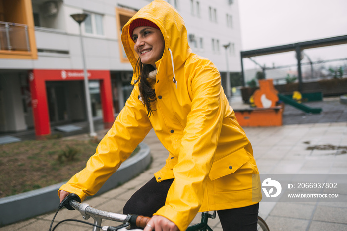 Smiling girl in yellow raincoat ride bicycle. Riding bicycle on rain day