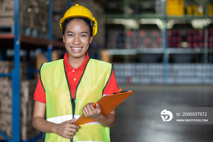 Portrait of African American smiling female warehouse worker with clipboard working and checking products or parcel goods on shelf pallet in industrial storage warehouse