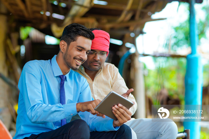 Young indian agronomist showing some detail to farmer in smartphone at dairy farm