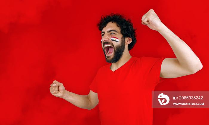 Sport fan screaming for the triumph of his team. Man with the flag of Egypt makeup on his face and red t-shirt and red background.